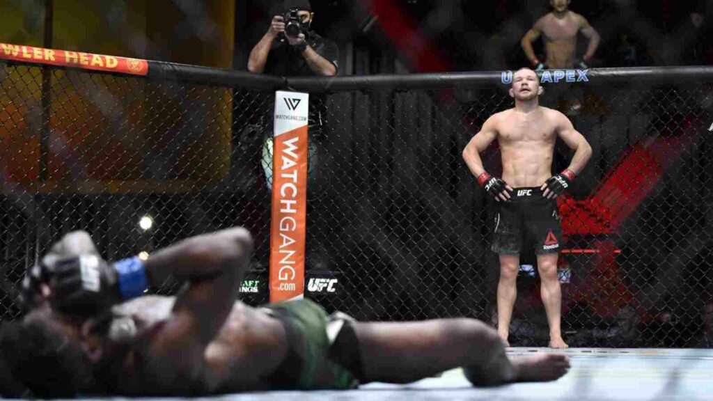 Petr Yan (R) stands over Aljamain Sterling writhing on the floor after the illegal knee