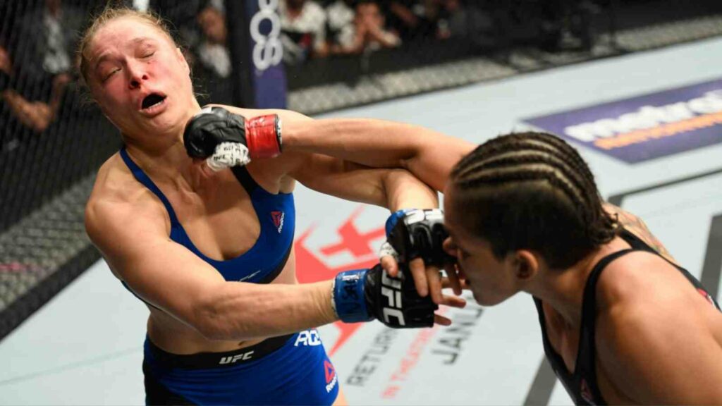 Ronda Rousey (in blue) gets hit by a nasty jab by Amanda Nunes (in black)